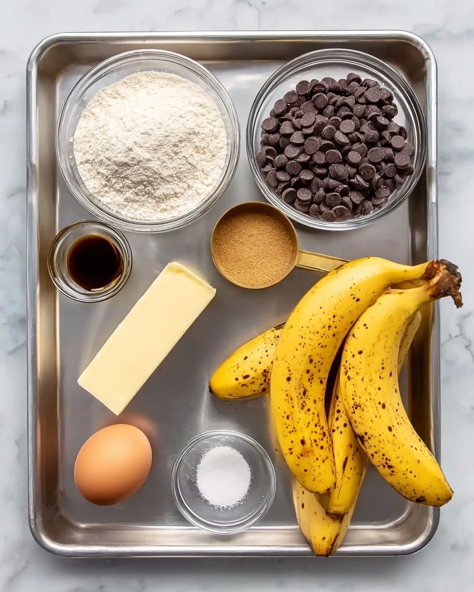 The image shows a silver baking tray on top of a white marbled surface, with several ingredients neatly placed inside. There are two ripe yellow bananas with brown spots on the right side. Above them is a small clear bowl full of mini dark brown chocolate chips. Next to the bananas and chocolate chips is a slightly bigger clear bowl filled with white flour. Above the flour is a brass measuring cup with light brown sugar. Below the sugar is a yellow stick of butter, next to an egg and a small clear bowl with dark vanilla liquid. In the middle of the tray is another small clear bowl with white salt. photo taken with an iphone --ar 4:5 --v 7