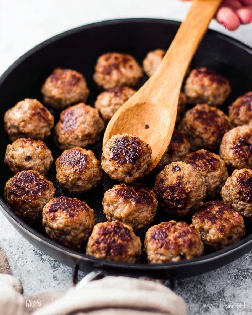 The image shows a close-up of many small, round brown meatballs in a dark pan. The meatballs have a crispy, textured outer layer with a mix of darker brown and lighter brown colors, showing they are cooked well. A wooden spoon is scooping several meatballs from the pan, held by a woman's hand that is partially visible. The background surface is white marbled texture, making the pan and meatballs stand out. photo taken with an iphone --ar 4:5 --v 7