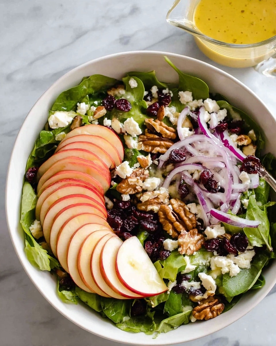 A white bowl filled with a fresh salad on a white marbled surface, showing a bottom layer of green leafy spinach. On top are thin, neatly arranged slices of red apple with white inside layers, scattered pieces of crunchy walnuts that are light brown, small dark red dried cranberries, thin slices of light purple onion, and crumbles of white feta cheese. A light yellow dressing is being poured over the salad, adding a shiny texture to the mix. Photo taken with an iphone --ar 4:5 --v 7