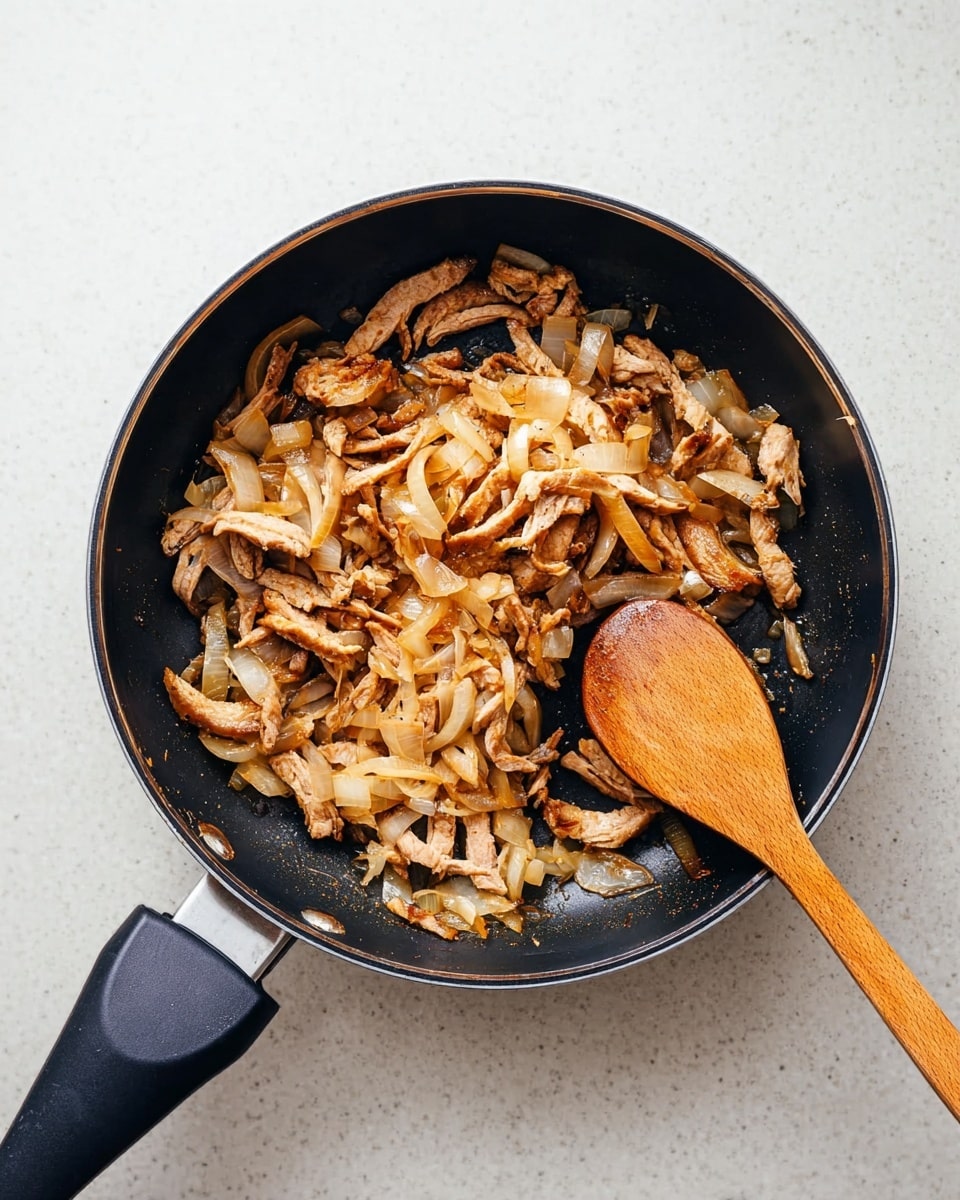 A black frying pan is shown from above on a white marbled surface, filled with many thin pieces of brown cooked meat and small light cooked onion pieces mixed in. A wooden spoon with a smooth, round head is resting inside the pan on the right side, touching the meat and onions. The meat has a slightly crispy texture with shades of light and dark brown, and the onion pieces are translucent with a pale yellow color. The pan's black handle extends outwards to the left side of the image. Photo taken with an iphone --ar 4:5 --v 7