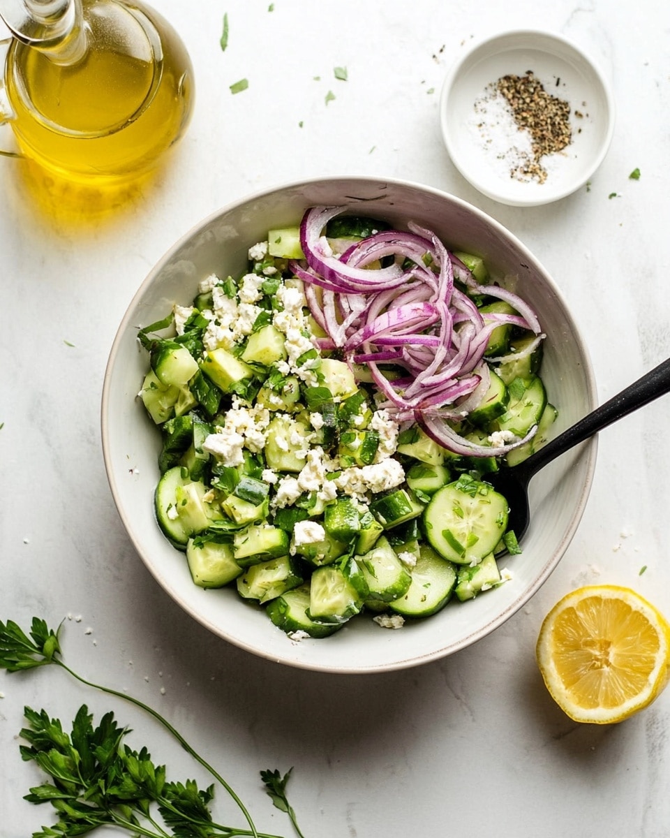 A white bowl filled with a fresh salad showing three main layers: the bottom layer is light green chopped cucumber chunks with a firm texture, the middle layer consists of thin, curved slices of purple-red onion, and the top layer has small white crumbly pieces of cheese along with chopped bright green parsley sprinkled all over. A black spoon rests inside the bowl, partially mixing the ingredients. Around the bowl, a clear glass bottle with yellow oil, a white small bowl containing salt and pepper, a half yellow lemon, and some parsley sprigs are placed on a white marbled surface. Photo taken with an iphone --ar 4:5 --v 7