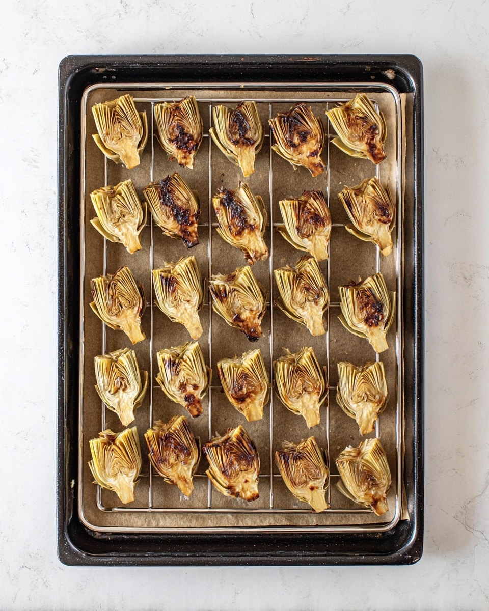 A black baking tray lined with brown parchment paper holds a silver cooling rack filled with 30 small artichoke halves, arranged in five rows of six. Each artichoke half has a golden brown color with darker charred spots, showing the layered texture of the leaves clearly visible. The tray rests on a white marbled surface, giving a clean background to the roasted artichokes. photo taken with an iphone --ar 4:5 --v 7