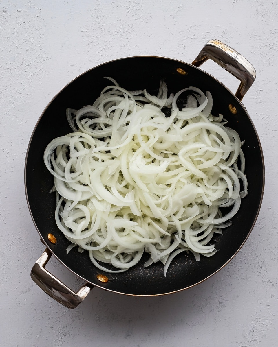 A black frying pan with two metal handles holds a single layer of thinly sliced white onions. The onions are pale, almost translucent, with soft curved shapes overlapping each other evenly across the pan. The pan sits on a white marbled surface, which adds a clean and simple background to the image. The onions have a light texture that looks fresh and uncooked. Photo taken with an iphone --ar 4:5 --v 7