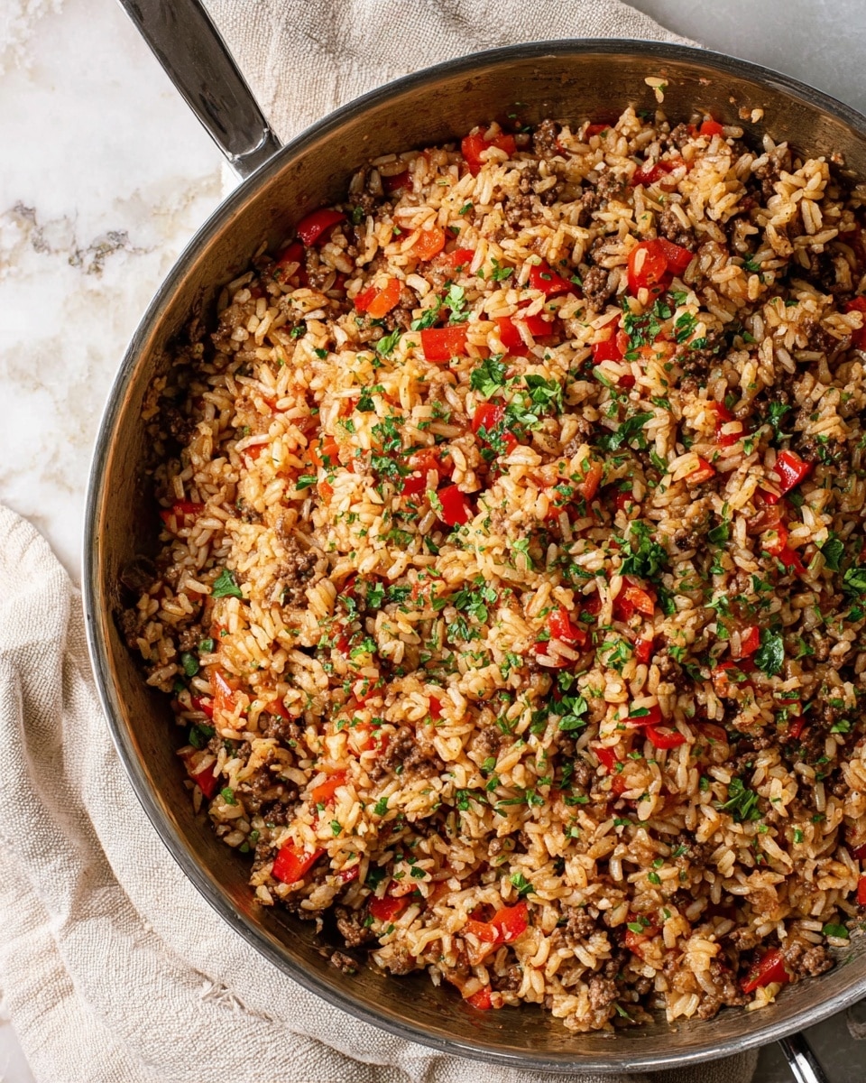 The image shows a close-up top view of a large metal pan filled with a mixed dish of cooked rice, small ground meat pieces, diced red bell peppers, and some chopped green herbs sprinkled on top. The colors are mostly light brown from the rice and meat, bright red from the peppers, and green from the herbs. The texture looks soft and mixed well, with the ingredients evenly spread in one layer inside the pan. The pan is set on a light beige cloth and a white marbled surface. photo taken with an iphone --ar 4:5 --v 7