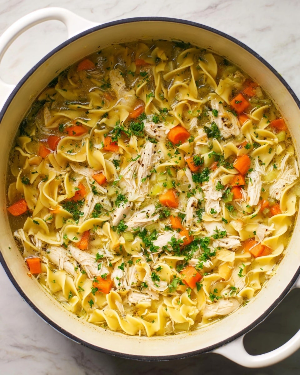 A large white pot filled with chicken noodle soup, showing three main layers: at the bottom, broth with small pieces of celery and onions creating a light golden base; above that, bright yellow wide egg noodles curling into waves and mixed with scattered chunks of shredded white chicken; on top, diced orange carrots and sprinkles of fresh chopped green herbs are spread evenly, adding color and texture contrast, all visible under soft lighting on a white marbled surface. photo taken with an iphone --ar 4:5 --v 7