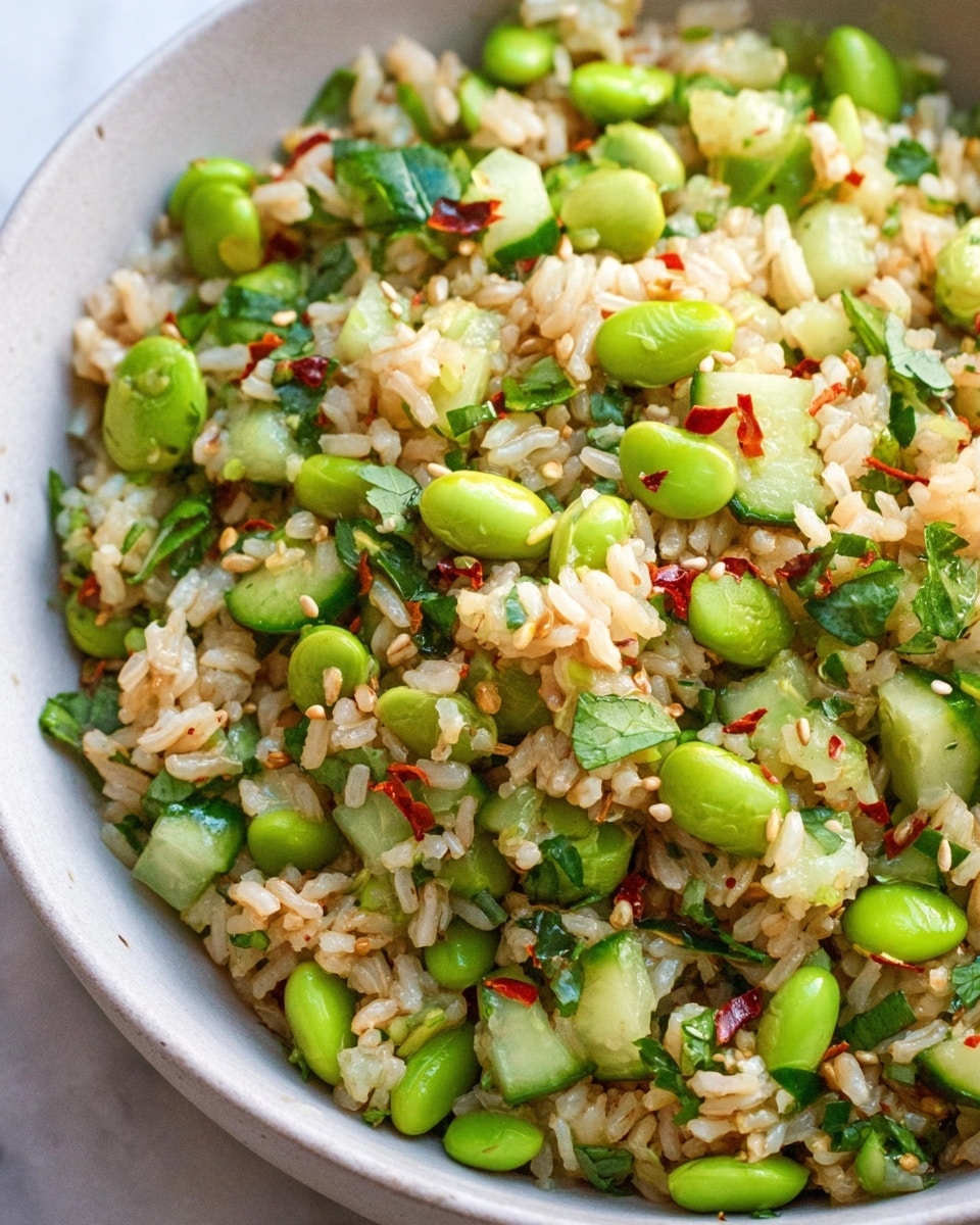 A close-up view of a bowl filled with cooked rice mixed with bright green edamame beans and small cubes of fresh cucumber. The rice grains are light brown and fluffy, speckled with sesame seeds and tiny red chili flakes. Fresh green herbs, possibly cilantro, are scattered throughout, adding pops of darker green. The bowl is white with a smooth texture, placed on a white marbled surface. The colors are fresh and vibrant, making the dish look healthy and appetizing. Photo taken with an iphone --ar 4:5 --v 7