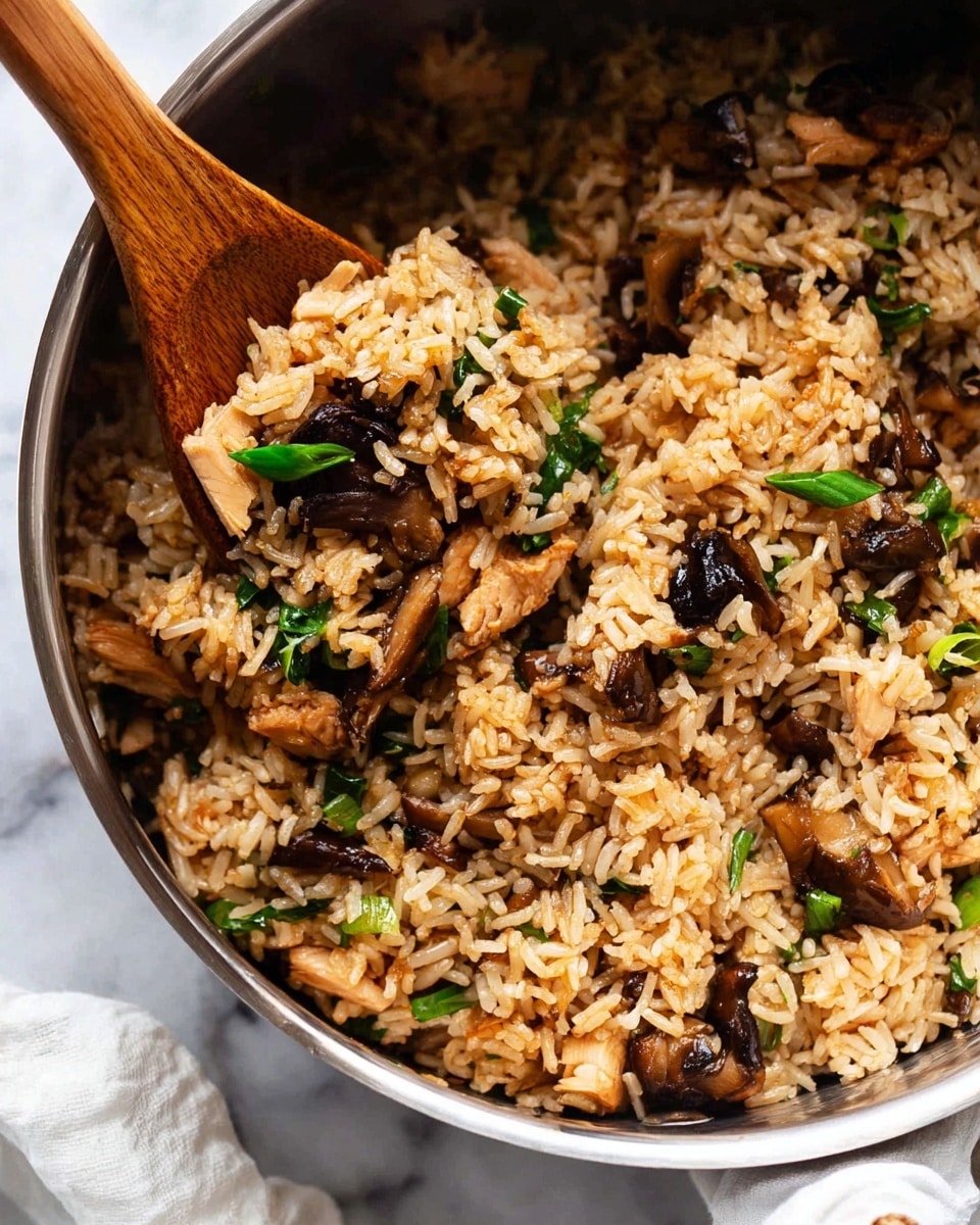 The image shows a close-up of a metal pot filled with cooked fried rice. The fried rice is light brown, mixed with pieces of dark shiitake mushrooms, small chunks of light beige chicken, and bright green slices of scallions. The texture looks moist and slightly shiny, with the rice grains separated. A wooden spatula is partly visible on the left side, lifting some of the rice. The background has a white marbled texture with a bit of a white cloth on the top right side. Photo taken with an iphone --ar 4:5 --v 7