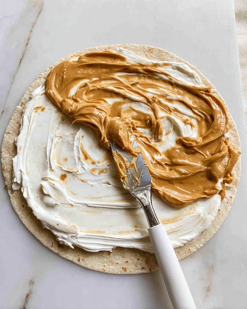 A flat, round light beige tortilla lies on a white marbled surface with two spread layers on top. The bottom layer is thick, smooth white cream cheese covering the whole tortilla. Above it, a light brown creamy peanut butter is partially spread, leaving some swirl marks where the layers mix. A silver spreader with a white handle is resting on the tortilla, with some peanut butter on its blade. photo taken with an iphone --ar 4:5 --v 7