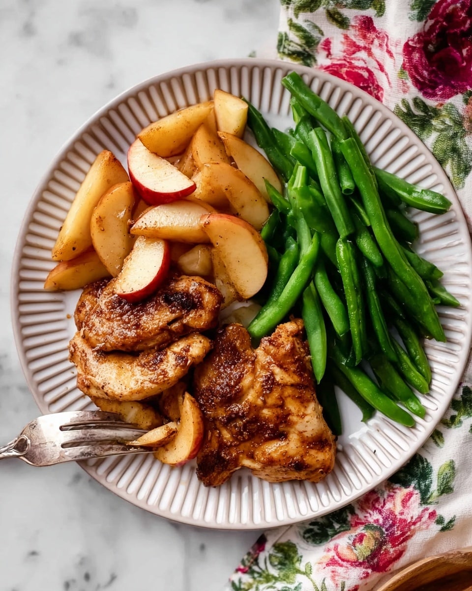 The image shows a close-up of a dish with seven golden-brown pieces of cooked chicken layered across the plate, each piece browned with a slightly crispy texture. Interspersed between and on top of the chicken pieces are thick slices of warm, pale yellow to orange apples with hints of red skin, carrying a lightly cooked softness. Scattered rosemary sprigs add green touches, enhancing the rustic and fresh look. A light, glossy sauce coats the entire dish, making the chicken and apples glisten slightly. The background is a white marbled texture. photo taken with an iphone --ar 4:5 --v 7