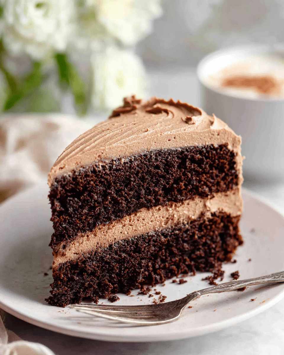 A slice of three-layer chocolate cake sits on a white plate with a soft white marbled background. The bottom and top layers are dark, rich, and moist chocolate cake with a rough, crumbly texture. Between these cake layers are two smooth and creamy layers of light brown chocolate frosting that look soft and thick. The outside of the cake is fully covered with the same frosting, swirled gently to add texture. In the background, there is a blurry white flower and a small white bowl with a drink or cream inside, topped with a sprinkle of brown powder. A silver fork rests on the plate next to the cake. photo taken with an iphone --ar 4:5 --v 7