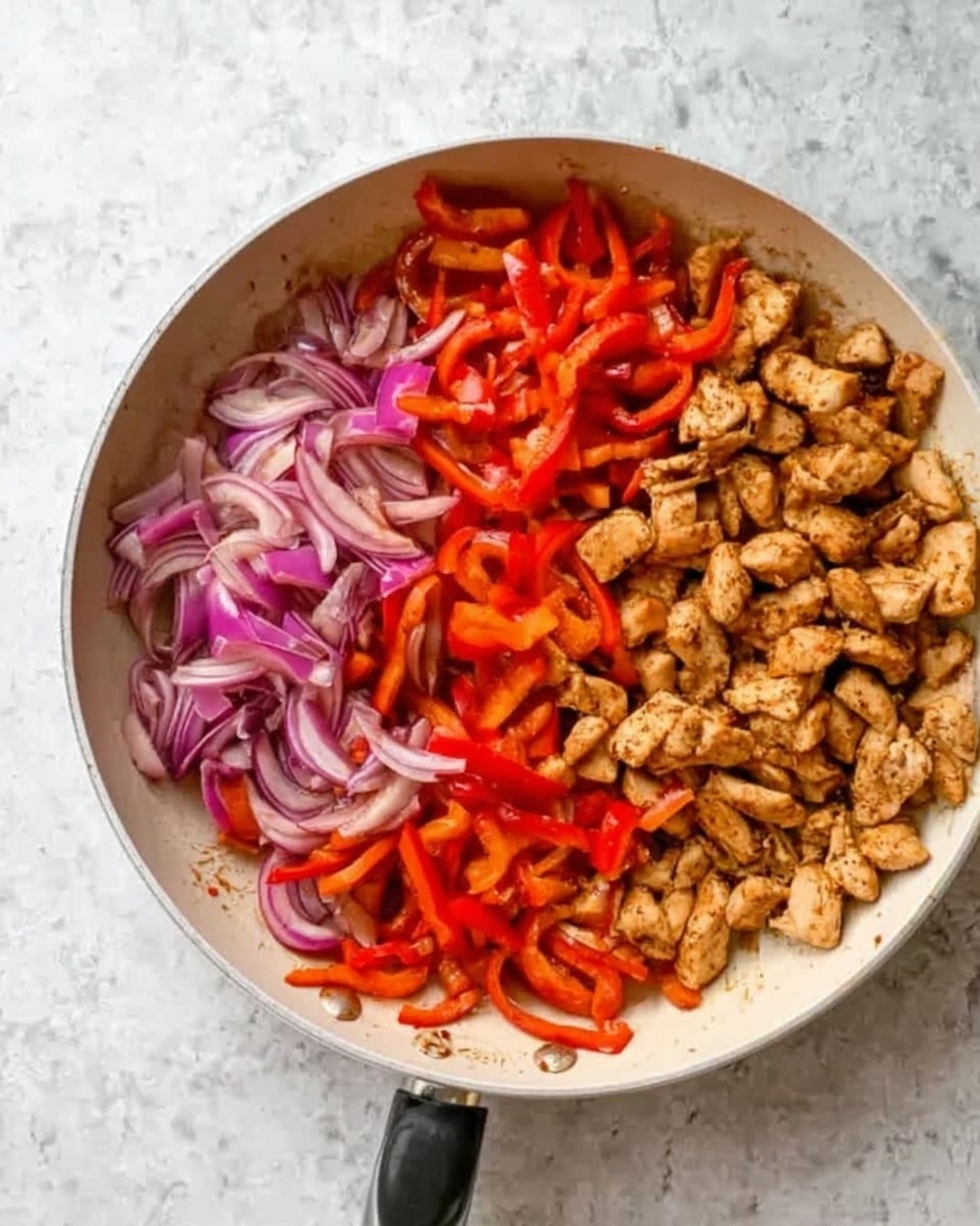 A white pan filled with two layers of food inside, on the left half there is a mix of sliced red bell peppers and thinly sliced red onions, showing bright reds and soft purples. On the right half, there are small pieces of cooked chicken colored light brown with a slightly rough texture. The pan is placed on a white marbled surface. photo taken with an iphone --ar 4:5 --v 7