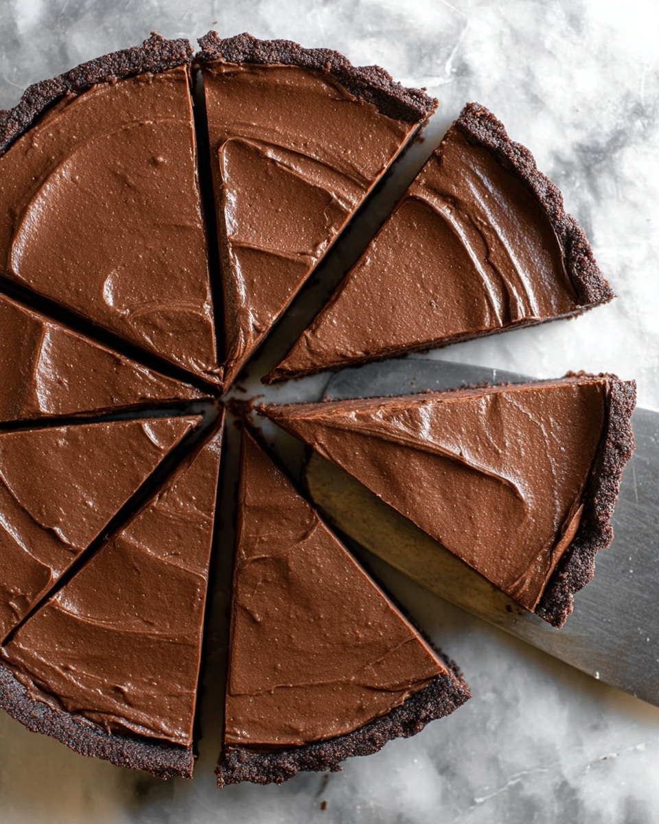 This image shows a chocolate tart sliced into eight pieces, with one slice being lifted by a metal spatula. The tart has two visible layers: a dark brown, slightly crumbly crust at the bottom and a smooth, thick layer of chocolate filling on top with a creamy texture and faint swirls. The tart is placed on a white marbled surface, and the chocolate filling has a rich, deep brown color that looks glossy under the light. photo taken with an iphone --ar 4:5 --v 7