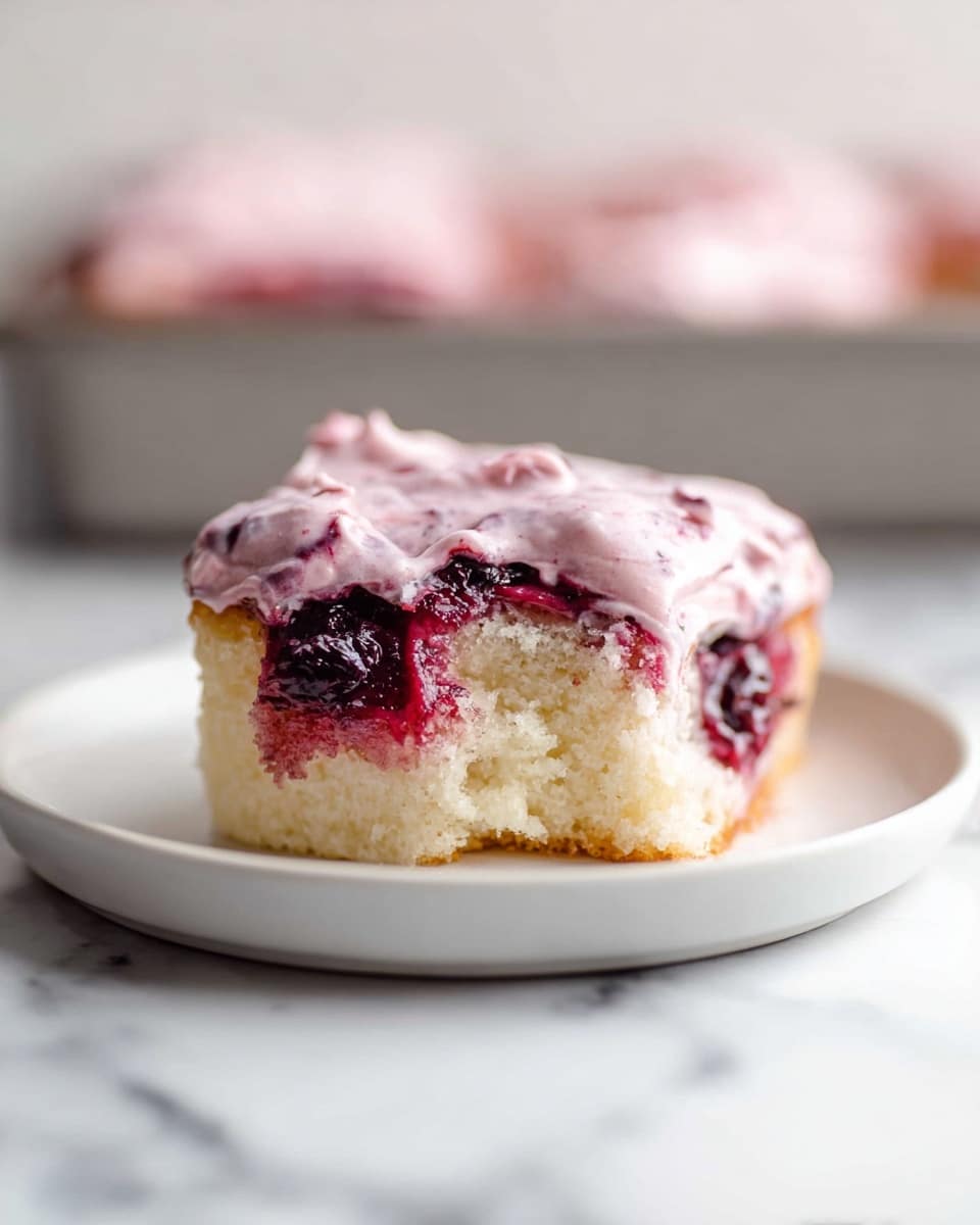 A single square piece of a soft, light-colored cake sits on a white plate, showing its fluffy and airy texture on the side where a bite is taken out. The cake is layered with a dark red and purple berry filling in the middle, which looks thick and juicy. On top, there is a thick layer of creamy pink frosting with small bits of berries visible inside, spreading unevenly over the edges. The background has a white marbled texture with an out-of-focus baking tray holding similar cakes. Photo taken with an iphone --ar 4:5 --v 7