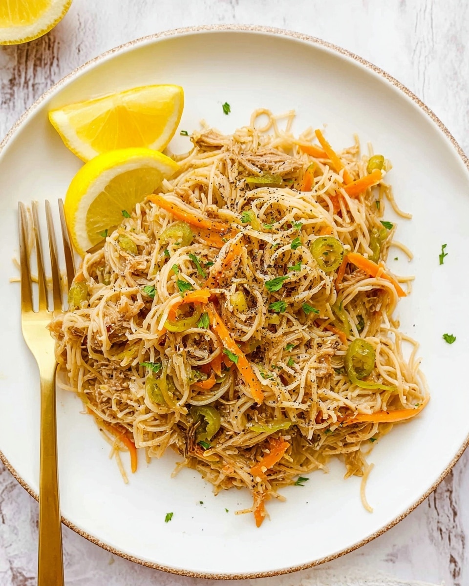 The image shows a white plate filled with a dish that has three main layers. The bottom layer is thin, light brown noodles with a soft texture spread evenly over the plate. Mixed in the noodles are thin orange carrot strips and light green chili pieces scattered throughout. On top of the noodles, there are small bits of shredded light meat, lightly mixed in. The dish is garnished with finely chopped green herbs and black pepper specks. Two lemon slices, one placed at the top edge and one at the right edge of the plate, add bright yellow colors. A gold fork rests on the left side of the plate. The background is a white marbled texture. Photo taken with an iphone --ar 4:5 --v 7