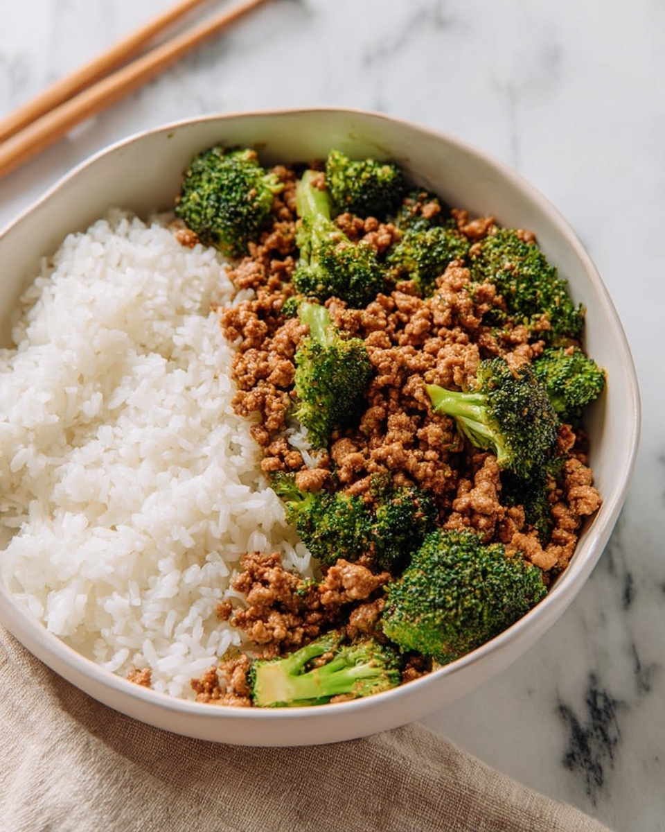 A white bowl filled with two main layers: on the left side, a layer of steamed white rice with a soft, fluffy texture and bright white color; on the right side, a layer of finely crumbled cooked ground meat mixed with vibrant green broccoli florets, both coated lightly with a brown sauce that gives a glossy look. The bowl sits on a white marbled surface, with a beige cloth and chopsticks slightly blurred in the background. photo taken with an iphone --ar 4:5 --v 7