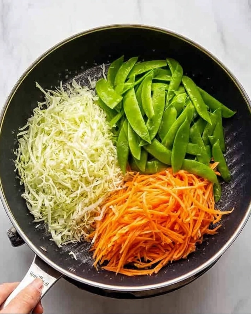 A top-down view of a round black frying pan on a white marbled surface, filled with three distinct layers of vegetables separated into sections. The first section contains finely shredded white cabbage with a light, crisp texture. Next to it is a cluster of bright green snow peas, smooth and fresh. The third section features thin, orange carrot strips arranged neatly. The pan's silver rim contrasts softly against the dark non-stick surface, and a woman's hand is gently holding the pan handle visible on the side. photo taken with an iphone --ar 4:5 --v 7