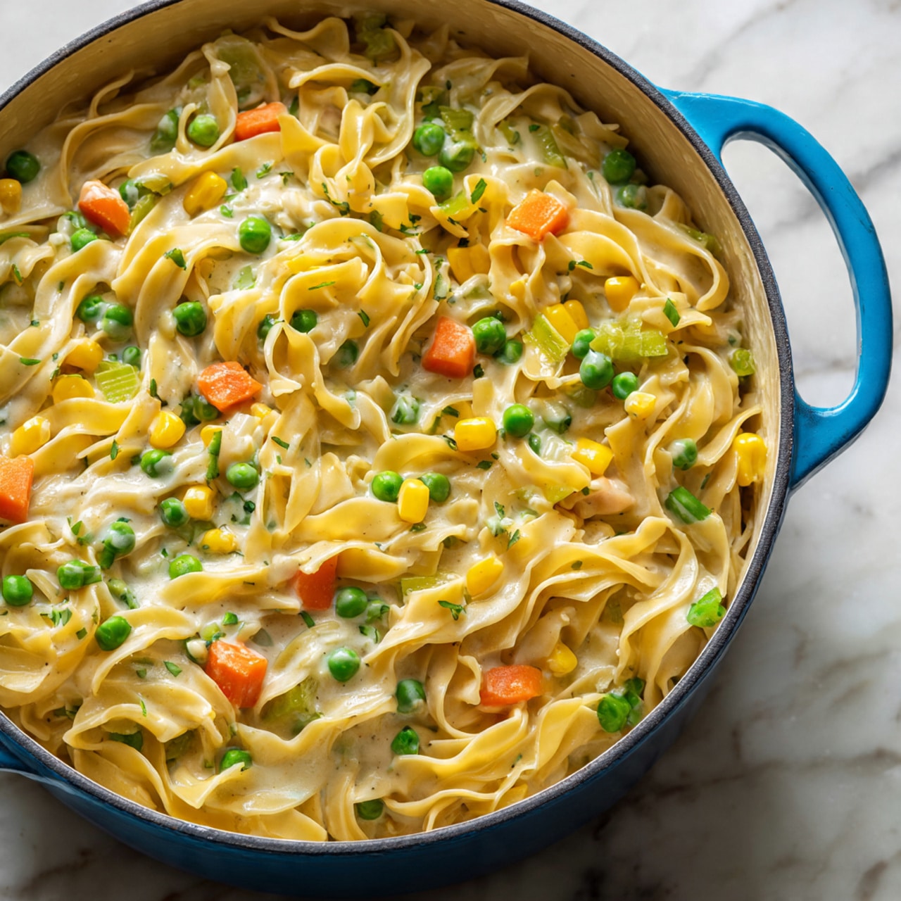 The image shows a close-up view of a blue pot filled with a creamy noodle dish. The dish has three main layers: wide, yellow egg noodles forming the base and top, a creamy light beige sauce as the middle layer, and mixed vegetables including bright green peas, yellow corn kernels, small pieces of pale green celery, and small orange carrot strips scattered evenly throughout. The pot is placed on a white marbled surface. The textures of the noodles look soft and slightly wavy, while the sauce appears smooth and thick. photo taken with an iphone --ar 4:5 --v 7