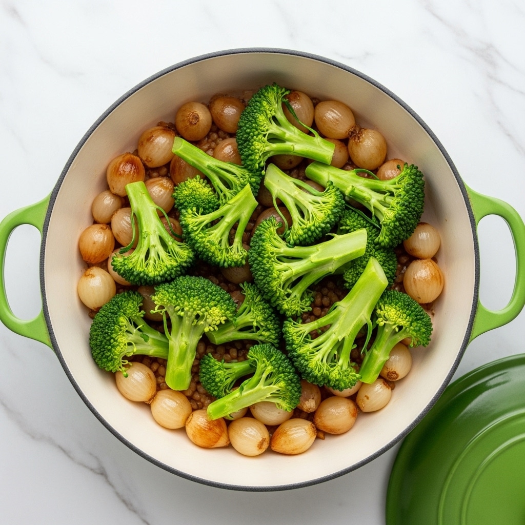 The image shows a white pot with green handles on a white marbled surface. Inside the pot, there is a base layer of small, soft, light brown grilled or cooked onions spread evenly. On top of this layer, bright green broccoli florets are placed, some showing their stalks and others their bushy tops, scattered naturally over the onions. The colors contrast between the golden onions and the fresh green broccoli. The pot is open, and the view is from above, capturing the vegetable mix clearly. photo taken with an iphone --ar 4:5 --v 7
