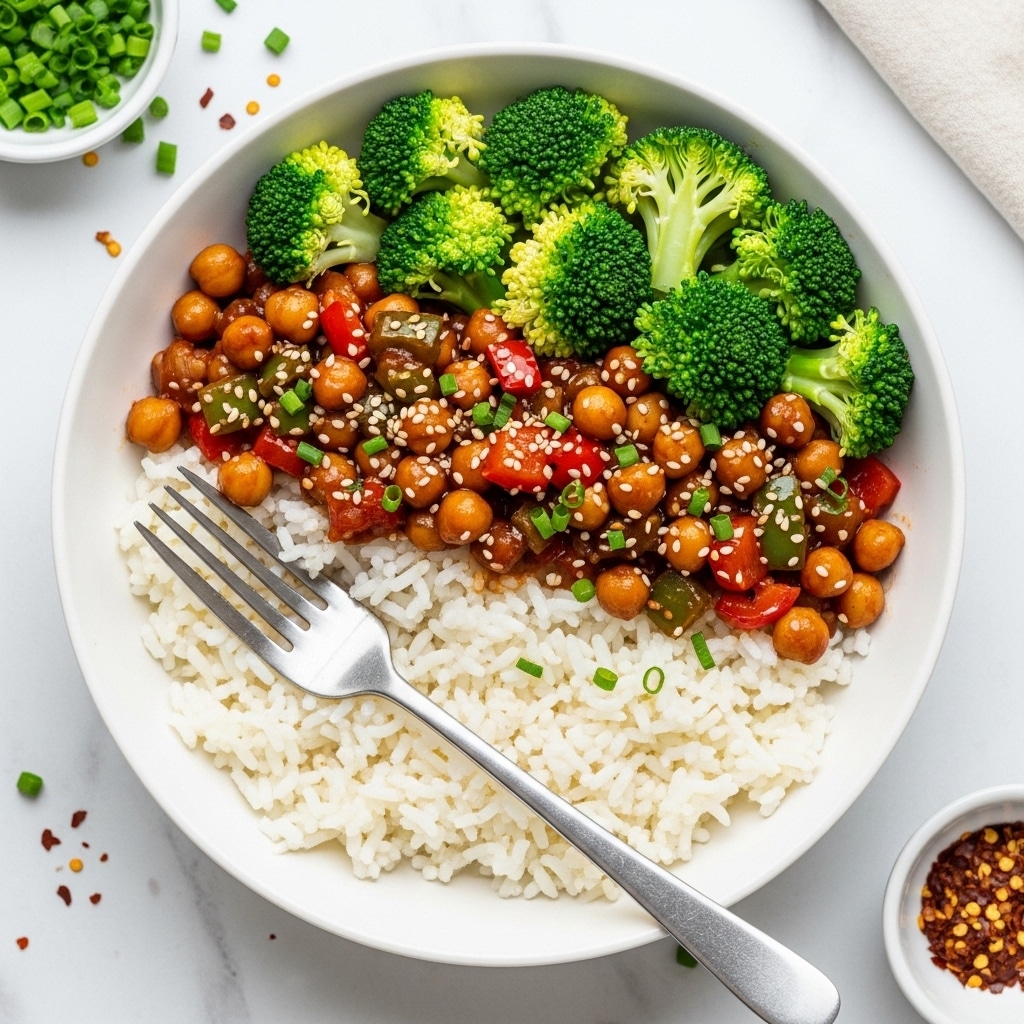 The image shows a white bowl with three main layers: at the bottom, soft white rice; on top of the rice, a colorful mix of chickpeas, diced red and green bell peppers in a glossy brown sauce sprinkled with green chives and small sesame seeds; and on one side, bright green steamed broccoli florets resting next to the chickpea mix. A silver fork is placed inside the bowl resting on the rice. The bowl is set on a white marbled surface with small bowls of chopped green chives and red chili flakes nearby. Photo taken with an iphone --ar 4:5 --v 7