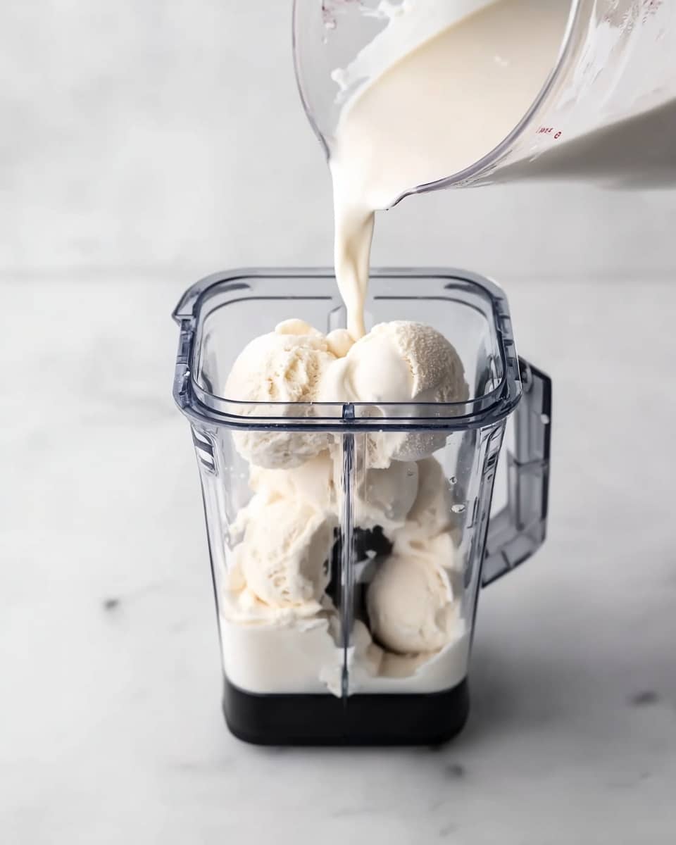 The image shows a clear blender container filled with several large scoops of white, creamy vanilla ice cream. A transparent measuring cup is tilted above the blender, pouring white milk into the container. The blender is set on a white marbled surface, and the scene is brightly lit with soft natural light, emphasizing the smooth texture of the ice cream and the flow of the milk. photo taken with an iphone --ar 4:5 --v 7