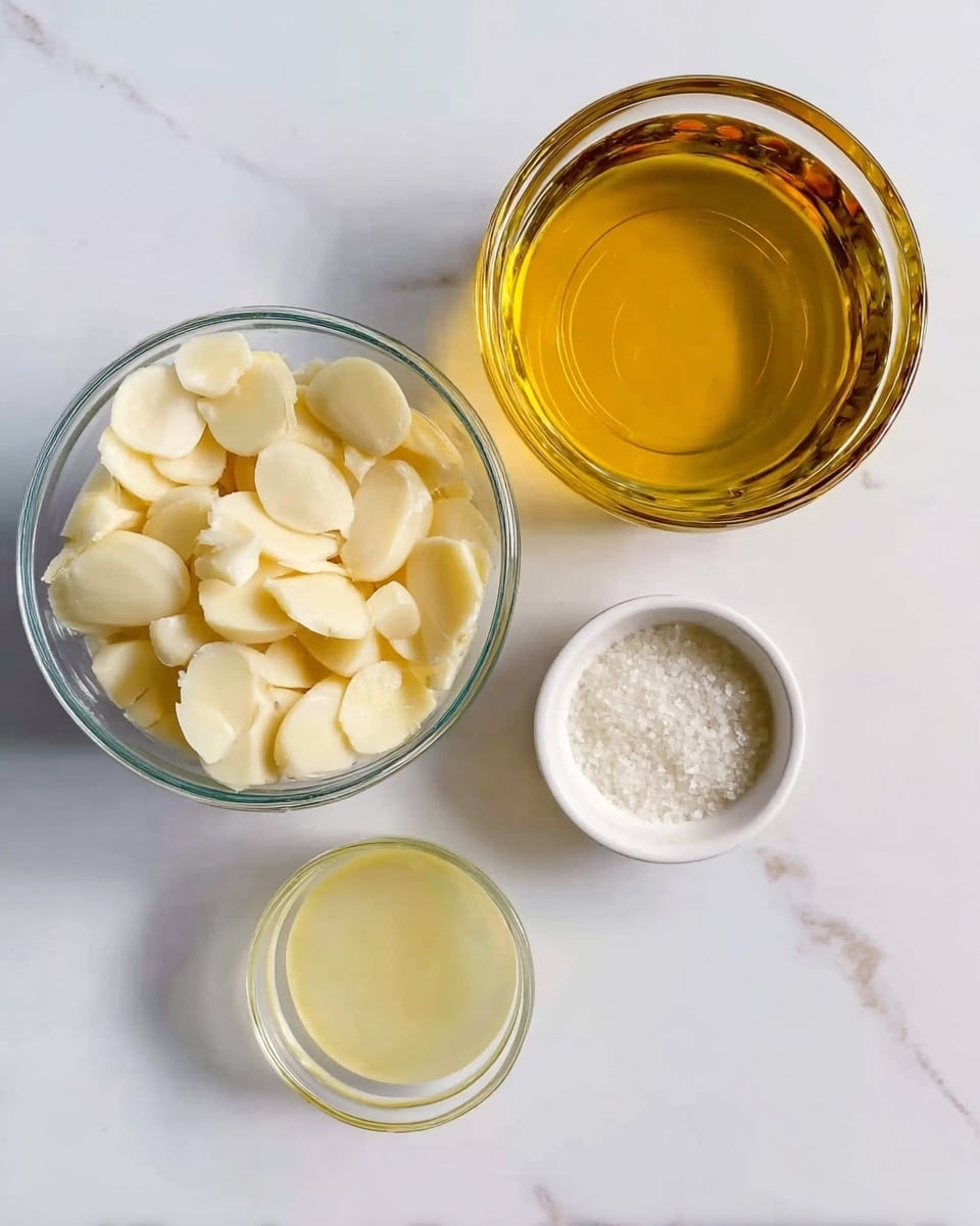 The image shows a top view of four glass and ceramic bowls placed on a white marbled surface. The largest bowl at the top right is filled with a golden-yellow liquid, likely oil, with clear and smooth texture. To its left, there is a clear glass bowl full of peeled garlic cloves, creamy white with smooth surfaces and some irregular shapes, filling the bowl. Below the garlic bowl, there is a smaller glass bowl containing a pale yellow translucent liquid, likely lemon juice, with a smooth surface. To the right of this bowl, there is a small white ceramic bowl filled with coarse white salt, showing grainy texture and small crystals. Everything is arranged neatly with bright, natural lighting. Photo taken with an iphone --ar 4:5 --v 7