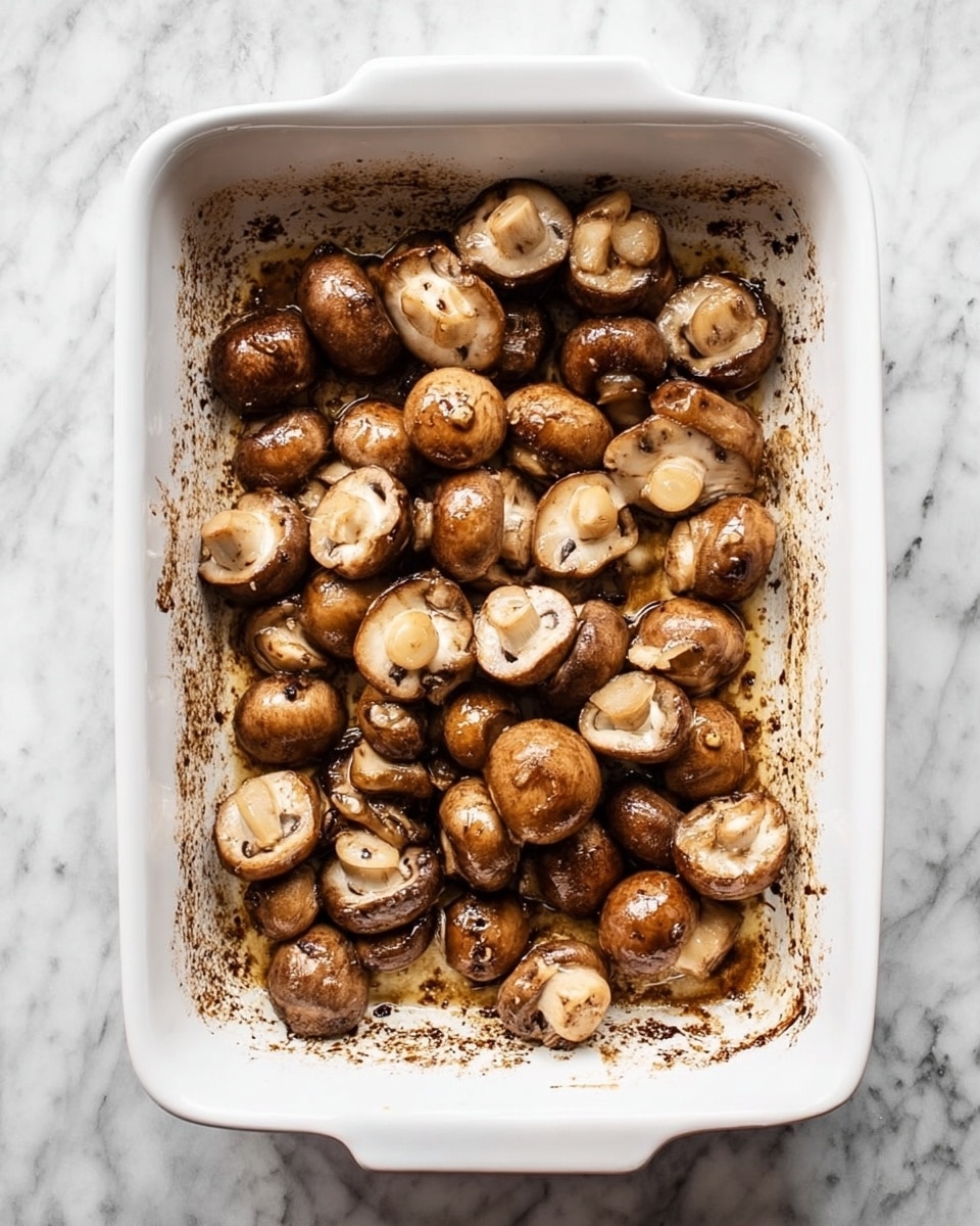 A white rectangular baking dish filled with a single layer of whole and halved brown mushrooms that have a slightly shiny texture, showing they are coated in oil or sauce; the mushrooms are arranged loosely with the cut sides up and down, and the dish has some dark brown spots of cooked sauce at the bottom. The dish sits on a white marbled surface. Photo taken with an iphone --ar 4:5 --v 7