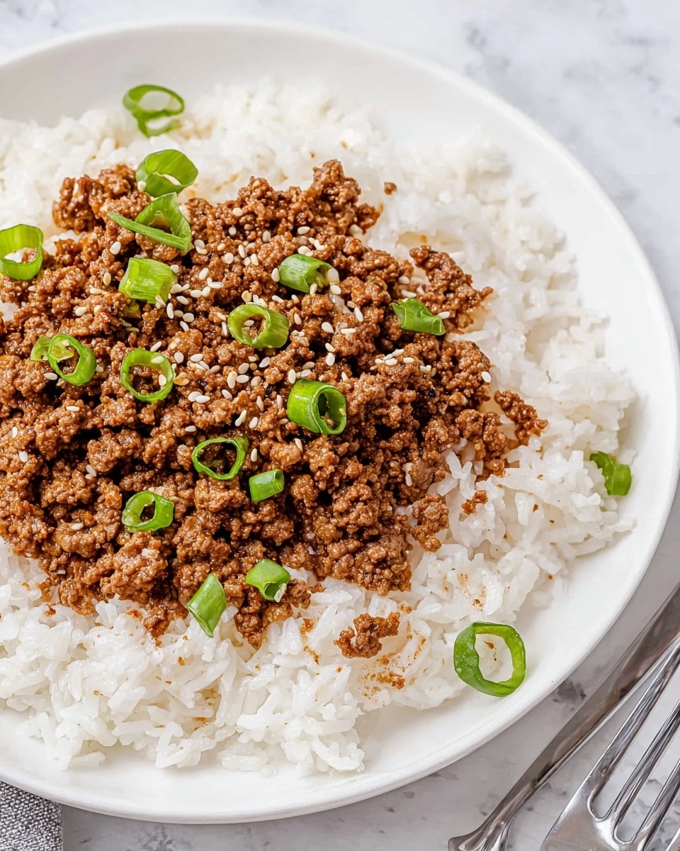A white plate holds a base layer of fluffy white rice with a soft texture, spread evenly across the plate. On top, there is a thick layer of finely cooked brown ground meat mixed with small golden bits, giving it a slightly crumbly texture. The meat is garnished with small rings of bright green sliced scallions and sprinkled with light tan sesame seeds, adding contrast. The plate is placed on a white marbled surface with a silver fork partially visible on the right side. Photo taken with an iphone --ar 4:5 --v 7