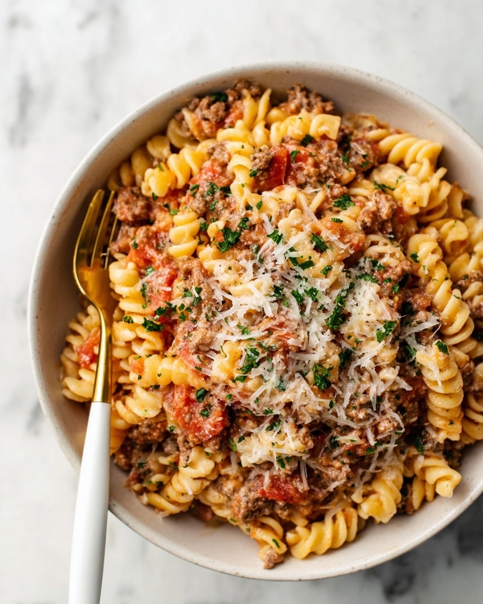 A close-up view of a bowl filled with creamy pasta that has three clear layers: a base of spiral pasta in pale yellow, mixed evenly with a light brown ground meat sauce containing soft red tomato pieces, all covered by a thin layer of grated white cheese and small green herb bits sprinkled across the top. A white fork with a gold head is placed on the left side inside the white bowl, resting on the pasta. The scene is set on a white marbled surface. Photo taken with an iphone --ar 4:5 --v 7