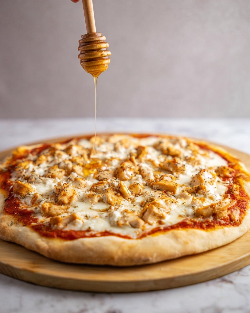 The image shows a round pizza with a thick, light golden crust resting on a wooden board. The first layer is bright red tomato sauce visible around the edges under the toppings. On top, there is a melted white cheese layer that covers the whole pizza. Scattered on the cheese are small chunks of cooked chicken that are lightly browned and seasoned with herbs sprinkled all over. Above the pizza, a woman's hand holds a wooden honey dipper with golden honey slowly dripping down onto the pizza. The background is a soft neutral color and the surface beneath the board is a white marbled texture. photo taken with an iphone --ar 4:5 --v 7
