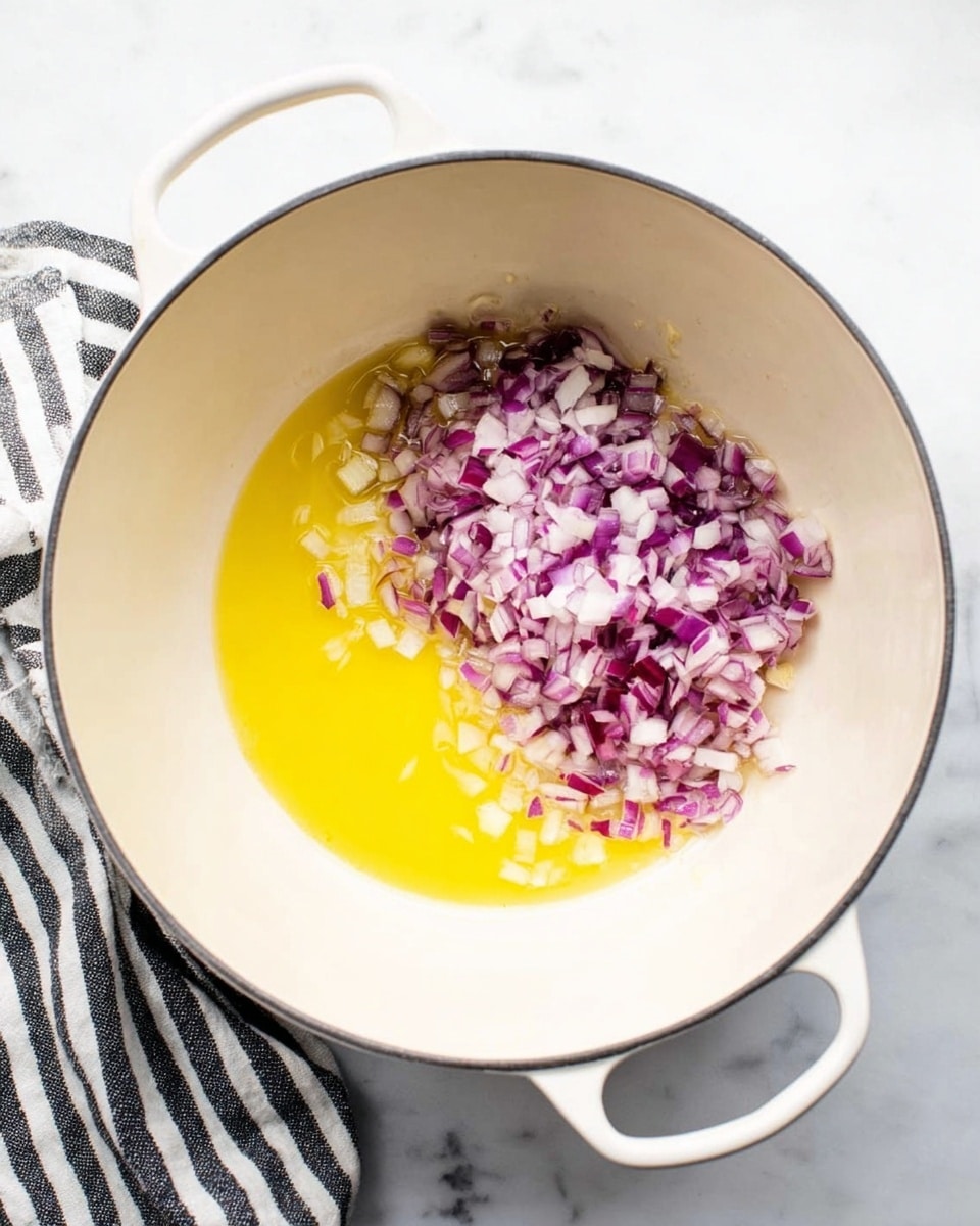 Inside a white pot with two handles, there is a layer of melted yellow butter covering the bottom. On one side, there is a pile of small chopped red onions with white and purple colors mixed. The pot is set on a white marbled surface, and a black and white striped cloth is placed next to the pot on the left. Photo taken with an iphone --ar 4:5 --v 7