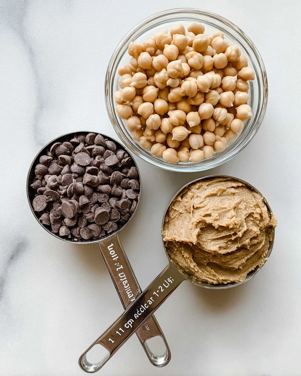The image shows three separate containers on a white marbled surface. On the top right, there is a clear glass bowl filled with light beige chickpeas. On the bottom left, there is a silver measuring cup with the label