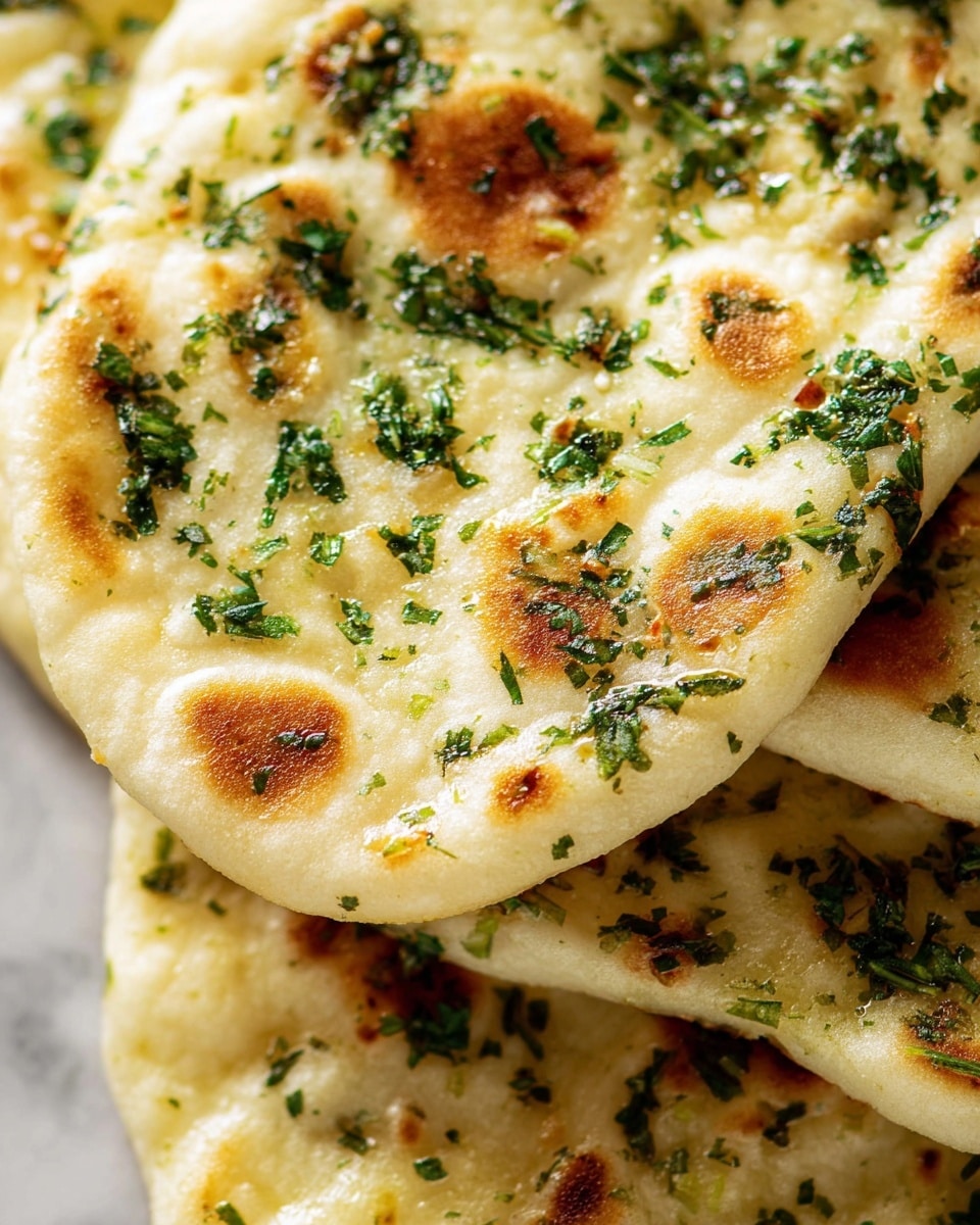 The image is a close-up of soft, flat rounds of bread stacked together showing light golden brown spots on their pale, creamy surfaces, topped with finely chopped fresh green herbs that are spread unevenly, adding little specks of dark and bright green over the bread layers. The texture of the bread looks slightly fluffy with small air pockets visible, while the herbs hint at a fresh, savory flavor. The background is a white marbled texture. photo taken with an iphone --ar 4:5 --v 7