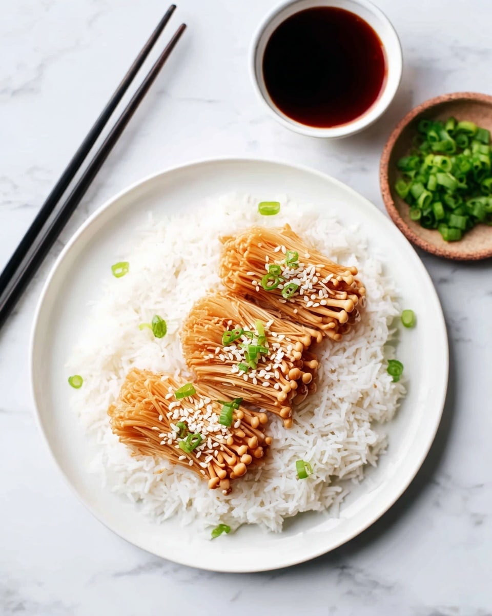 A white round plate holds a neat layer of fluffy white rice as the base. On top, there are three clusters of light brown enoki mushrooms, cooked and laid side by side, each topped with small white sesame seeds and chopped bright green onions. To the right side of the plate, there is a small white bowl filled with dark soy sauce and a small brown bowl with extra chopped green onions. Two black chopsticks rest on the left edge of the plate, all set on a white marbled surface. Photo taken with an iphone --ar 4:5 --v 7