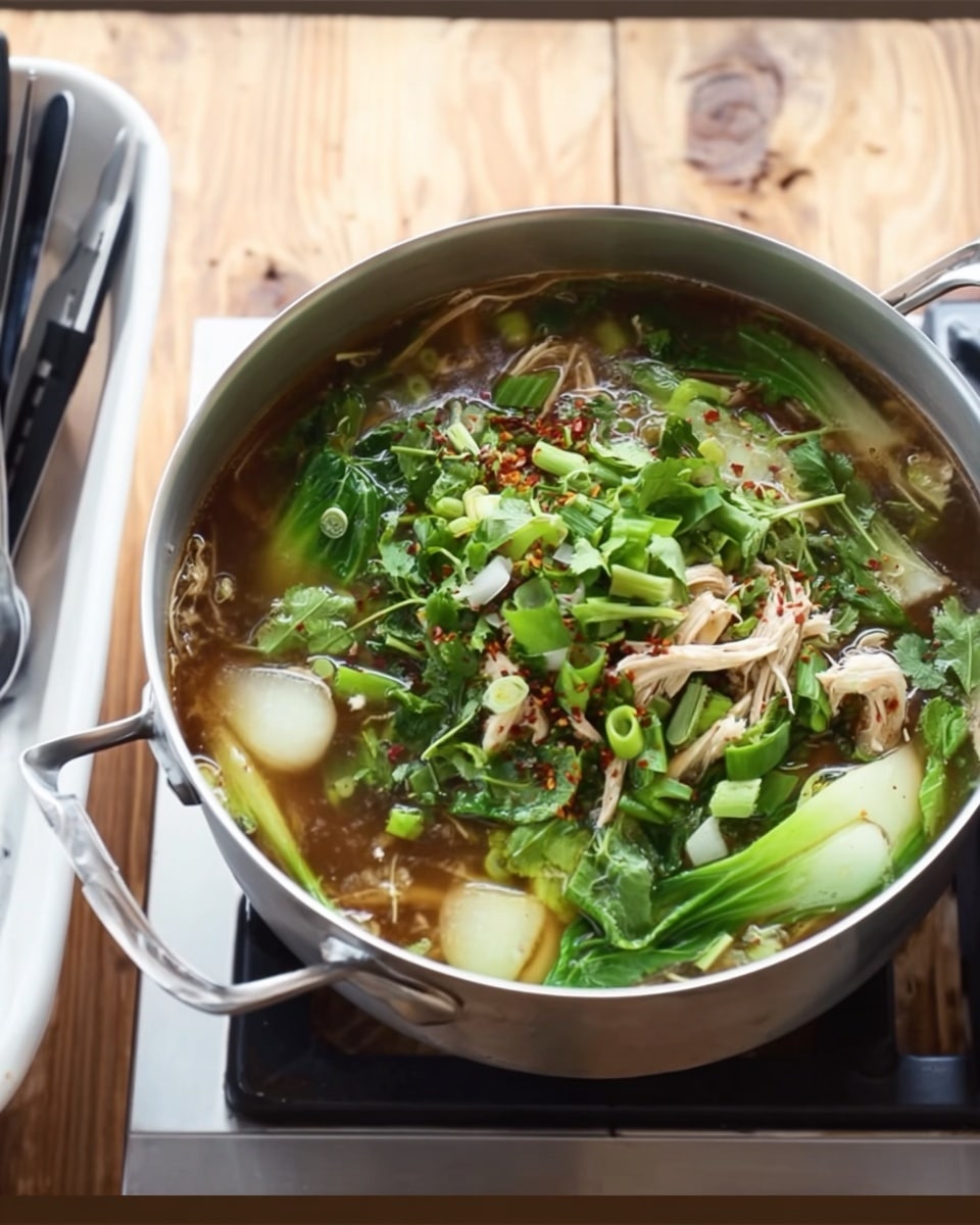 A metal pot filled with a soup that has several layers; at the bottom, clear brown broth with bits of herbs and chopped green onions, above that leafy green bok choy pieces spread around, some white and light green inner parts of the bok choy visible, topped with light-colored shredded chicken and scattered bright green cilantro leaves, with thin noodles mixed in the broth and some red chili flakes sprinkled on top. The pot is placed on a stove with a wooden surface background, next to a white tray holding black and white cooking utensils. Photo taken with an iphone --ar 4:5 --v 7