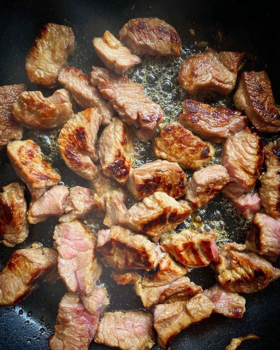 The image shows many pieces of meat cooking in a pan. The meat pieces vary in size and shape, with light brown color on most parts and some pink areas showing they are partly cooked. Some pieces have darker, crispy grill marks, showing a mix of soft and slightly charred texture. The pan surface is black and there is some bubbling oil around the meat, adding shiny spots. The overall look is that of meat frying and starting to turn cooked with a mix of colors and textures visible. photo taken with an iphone --ar 4:5 --v 7