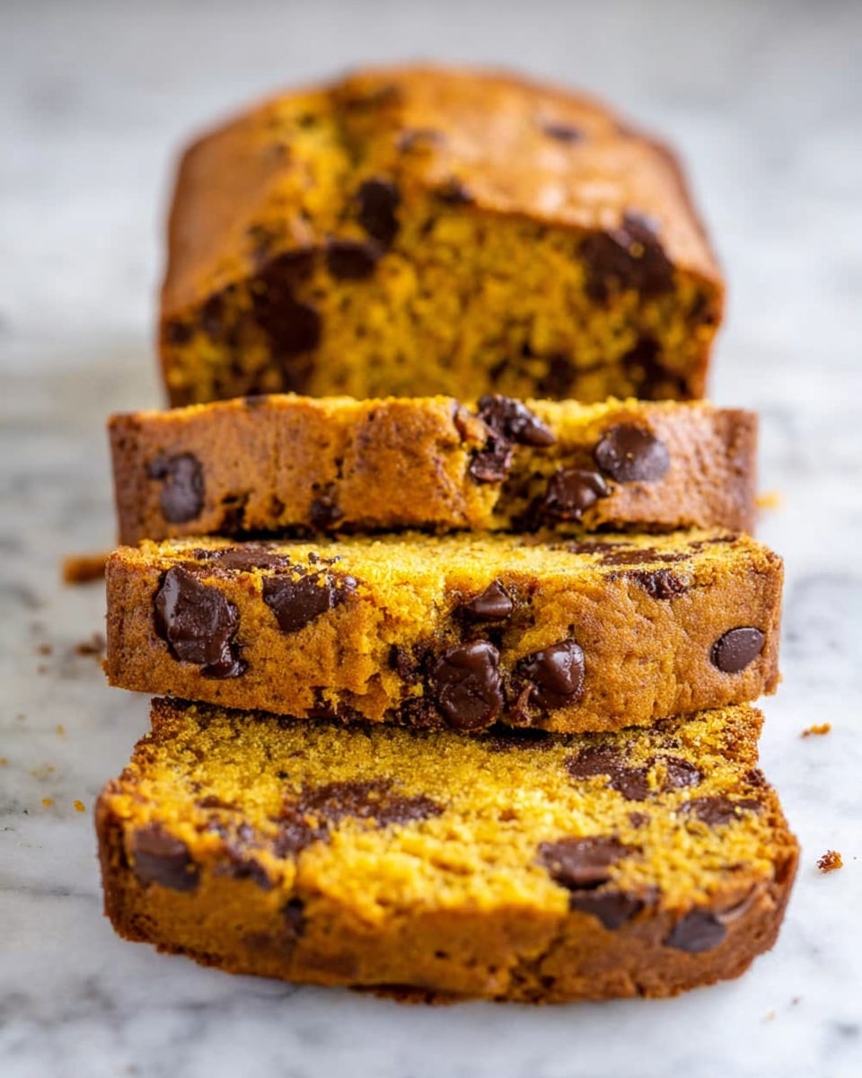 The image shows a loaf of pumpkin bread with chocolate chips, sliced into three pieces arranged in a row on a white marbled surface. The bread loaf is golden brown on the outside with a soft, moist orange interior spotted with dark brown chocolate chips. The slices are thick and reveal the dense texture of the bread, with chocolate chips evenly spread inside. The top of the loaf is slightly cracked, showing its tender crumb inside. Photo taken with an iphone --ar 4:5 --v 7