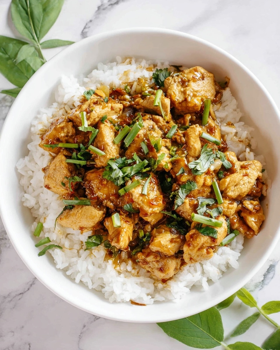 A white bowl filled with a layer of fluffy white rice at the bottom, topped with a thick layer of cooked chicken pieces coated in a shiny brown sauce mixed with bits of sautéed onions and green herbs scattered throughout. Fresh green leafy herbs are sprinkled on top, adding brightness and texture. The bowl is placed on a white marbled surface with some green leaves visible around the edges. photo taken with an iphone --ar 4:5 --v 7