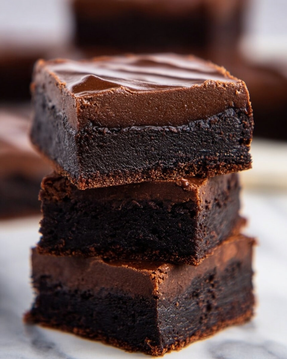 This image shows a stack of three thick, square chocolate brownies with two clear layers in each piece a bottom dark, dense, and slightly crumbly layer, topped by a smooth, firm chocolate layer with subtle texture on top. The edges are clean but slightly rough, and the brownies have a rich dark brown color. In the blurred background, more brownies can be seen on a white marbled surface. photo taken with an iphone --ar 4:5 --v 7