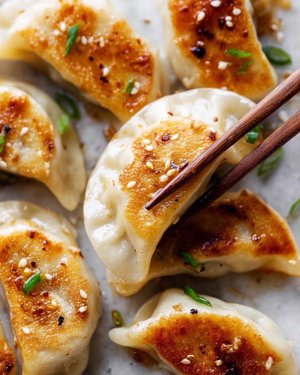 The image shows several pan-fried dumplings with golden brown crispy spots on their smooth, white dough. Each dumpling has a slightly curved, crescent shape with pleated edges. The dumplings are sprinkled with small white sesame seeds and tiny green onion pieces. A pair of brown chopsticks is holding one dumpling in the center. The dumplings are placed on a white marbled surface that adds a clean look to the picture. photo taken with an iphone --ar 4:5 --v 7