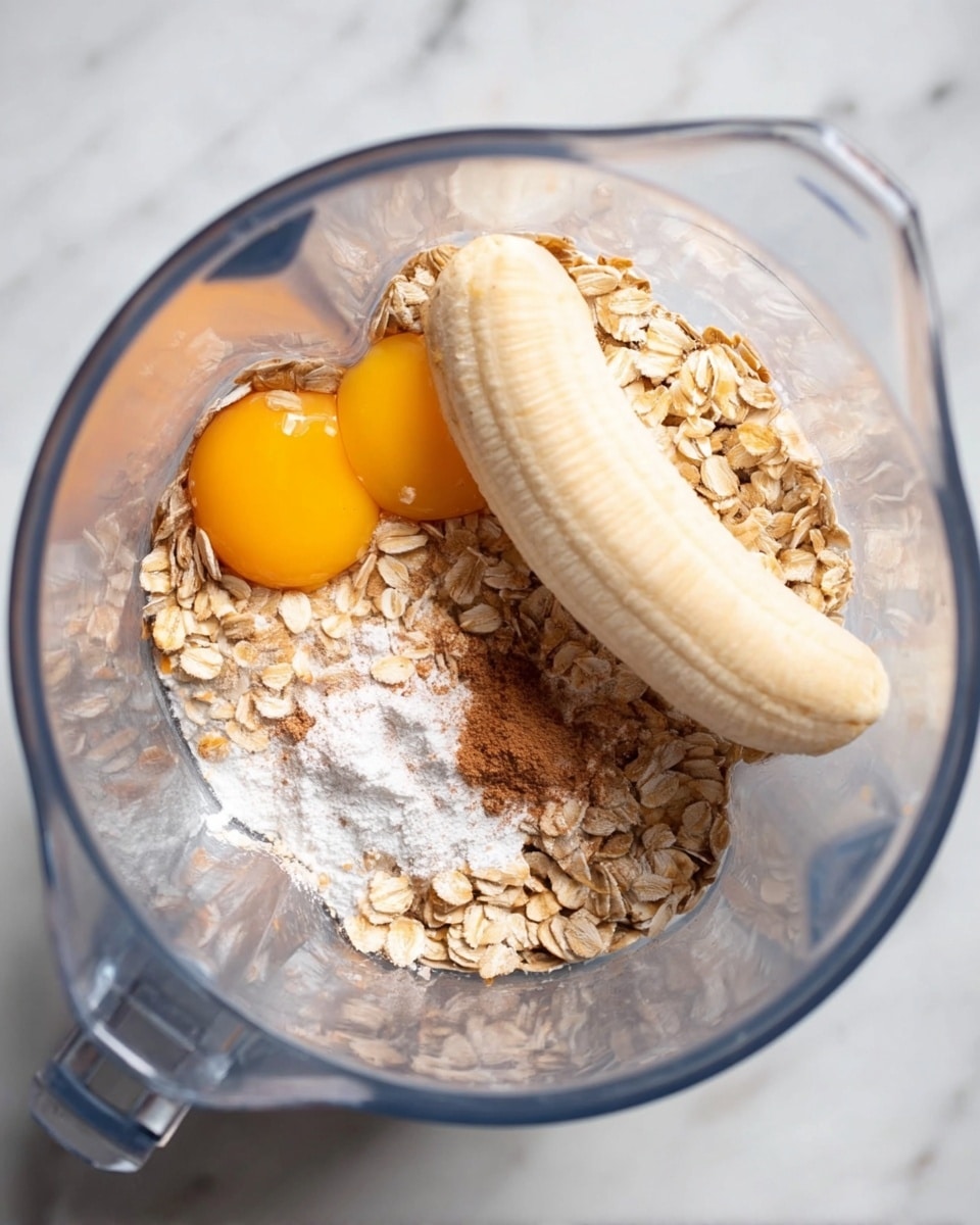 Inside a clear blender jar, there is one whole peeled banana lying on top of other ingredients. Beneath the banana, two raw egg yolks with bright yellow-orange color sit near the back. Around the banana, there are light tan rolled oats scattered on the bottom of the blender. On top of the oats and banana, there is a sprinkle of white powder, likely baking soda or powder, along with a small amount of brown spice powder, probably cinnamon. The background is a white marbled texture. photo taken with an iphone --ar 4:5 --v 7
