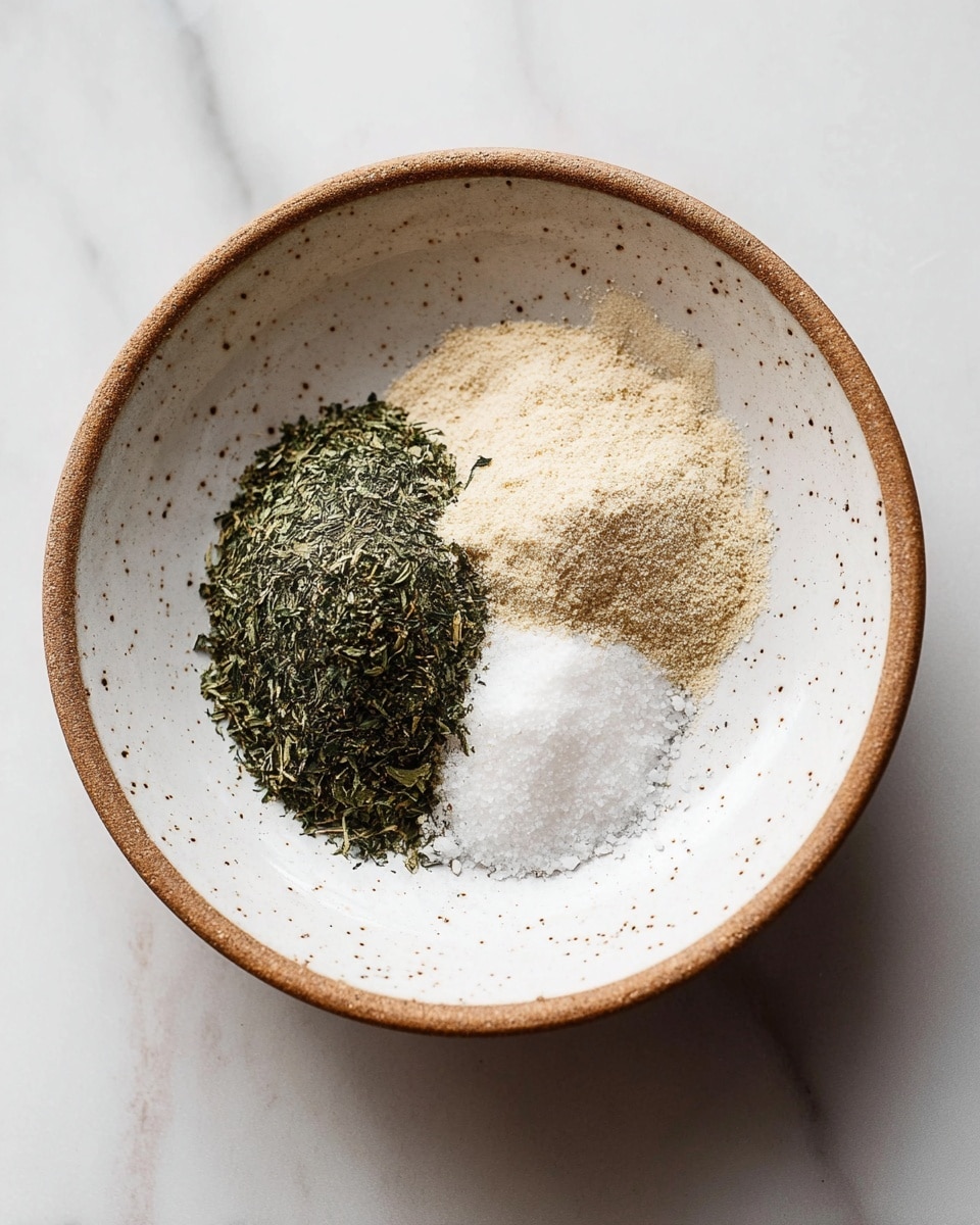 A white speckled bowl with a brown rim sits on a white marbled surface. Inside the bowl are three piles of spices arranged in a triangular shape: a dark green leafy herb on the left side, a light beige powder spice on the top right, and a small mound of white coarse salt on the bottom. The textures vary with the leafy herbs appearing dry and crumbly, the powder smooth and fine, and the salt looking granular and rough. photo taken with an iphone --ar 4:5 --v 7