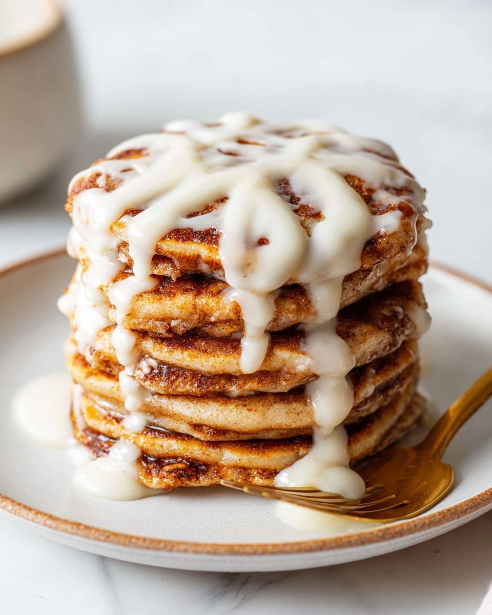 A stack of six thick pancakes sits in the center of a white plate on a white marbled surface. Each pancake has a golden-brown color with visible swirls of cinnamon within the layers, giving them a textured look. A generous amount of creamy white icing is drizzled over the top pancake, dripping down the sides onto the lower pancakes and plate. A fork with a golden handle rests at the edge of the plate, complementing the warm tones of the pancakes. photo taken with an iphone --ar 4:5 --v 7