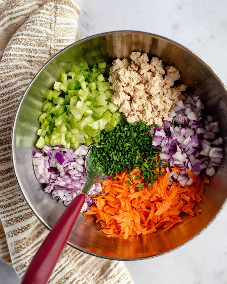 A shiny metal bowl holds five separate piles of fresh ingredients: bright green diced celery on the left, finely chopped purple and white onion at the top, pale beige crumbled tofu on the top right, thin bright orange shredded carrots on the bottom left, and finely chopped green chives on the bottom right. A spoon with a red handle rests inside the bowl, mostly on the right side. The bowl is placed on a white marbled surface next to a beige and white striped cloth. photo taken with an iphone --ar 4:5 --v 7