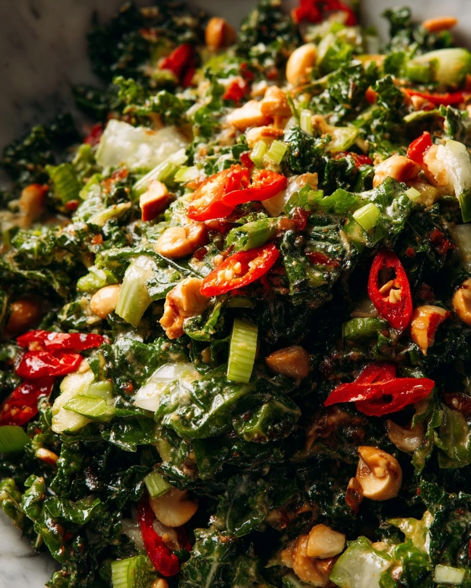 The image shows a close-up view of a mixed salad with several layers of ingredients. The base layer is made of finely chopped dark green kale and light green scallions, giving a leafy and fresh texture. Scattered on top are chunks of light brown nuts, adding a crunchy texture. Interspersed throughout the mix are bright red slices of chili peppers, contributing vibrant color contrast. A light, slightly frothy dressing coats the ingredients, giving a glossy and moist look. The whole salad sits on a white marbled surface, making the colors pop clearly. photo taken with an iphone --ar 4:5 --v 7