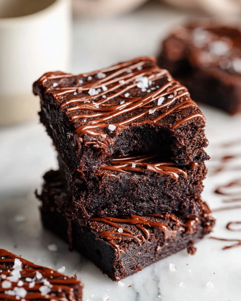 This image shows a close-up of one thick square brownie piece on crumpled white parchment paper over a white marbled surface. The brownie has a rich, dark brown color with a slightly rough texture and appears moist inside. On top, there are even lines of smooth, glossy chocolate drizzle running diagonally, with small flakes of white sea salt scattered across. Around the main brownie, parts of two other brownies are slightly visible, also with the same chocolate drizzle. Photo taken with an iphone --ar 4:5 --v 7
