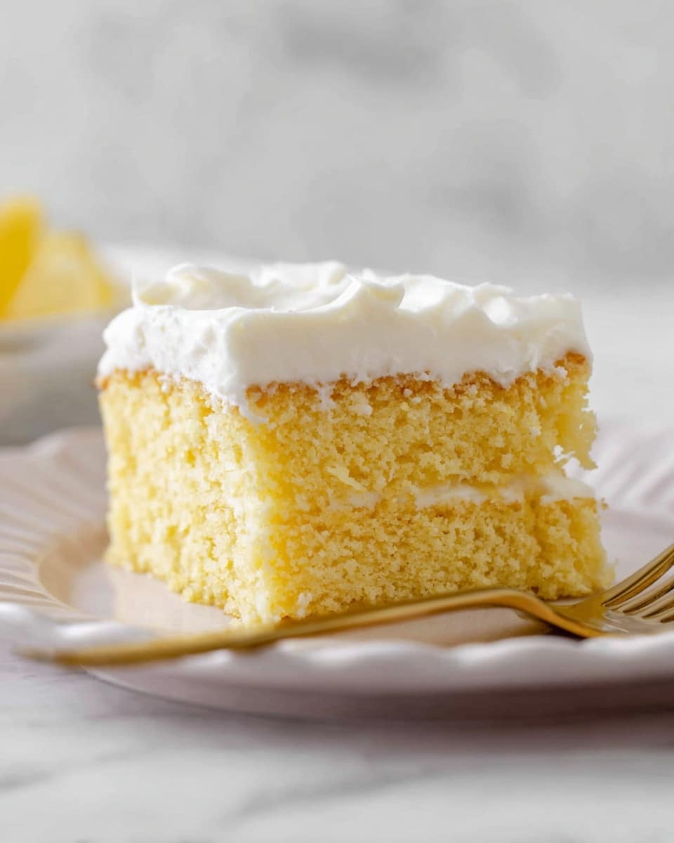 A piece of yellow sponge cake with a soft crumb texture sits on a white plate with slight waves on the edge. The cake has two layers: a thick, moist yellow base layer and a smooth, thick white frosting layer on top. The frosting looks creamy and softly spread with gentle waves. In front of the plate, there is a small part of a gold-colored fork resting. The background is a white marbled surface with soft lighting. photo taken with an iphone --ar 4:5 --v 7