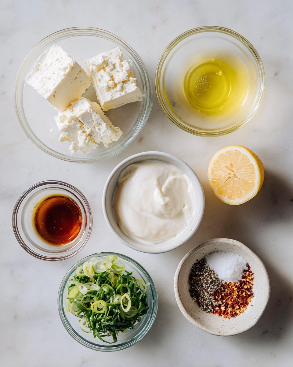 The image shows several small clear bowls and a white speckled bowl placed on a white marbled surface. Starting from the top left, there are three blocks of white feta cheese in a clear bowl with a crumbly texture. Next to it on the right is a clear bowl with a light yellow liquid, likely olive oil. Below the cheese is a white round container filled with a smooth textured white cream or yogurt. To the right of the oil, there is a halved lemon showing its bright yellow inner flesh. Below the oil is a small clear bowl containing a dark amber liquid. At the bottom left, a clear bowl holds chopped green herbs and spring onions with a leafy and fresh texture. On the bottom right, a white speckled bowl contains a mix of coarse salt, black pepper, chili flakes, and dried onion powder, creating a mix of white, black, red, and beige colors. The lighting is soft and natural, enhancing the fresh and simple look of the ingredients photo taken with an iphone --ar 4:5 --v 7