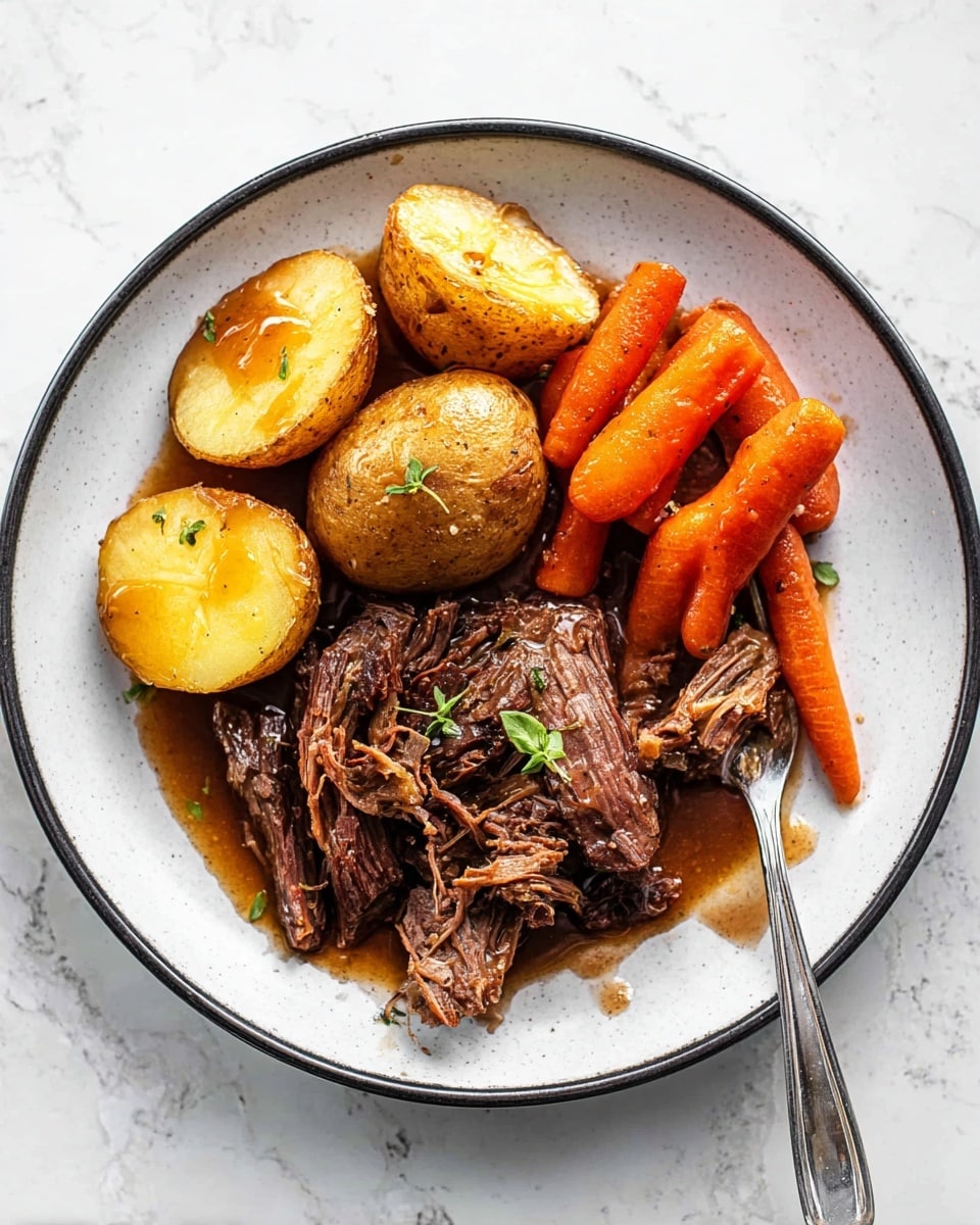 A white plate with a dark rim holds a serving of slow-cooked beef at the bottom, dark brown and shredded with visible texture, topped with a small sprig of green herb. Above the beef, there are five halved and whole golden brown potatoes with a soft yellow inside, mixed with bright orange baby carrots set around the edges. The vegetables and meat are lightly covered in a shiny brown gravy, with a silver fork resting on the right side of the plate. The whole setup sits on a white marbled surface. Photo taken with an iphone --ar 4:5 --v 7