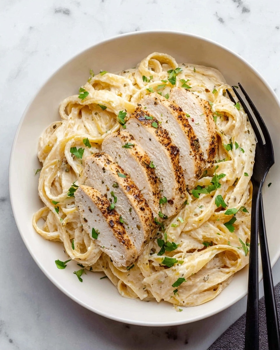 A white bowl sits on a white marbled surface, filled with creamy fettuccine pasta that has a smooth, light-colored sauce coating each strand. On top of the pasta, there are four slices of cooked chicken arranged in a neat row, showing a golden-brown sear on the outside and a juicy, pale interior. Small green herb pieces are sprinkled over both the pasta and chicken, adding a fresh contrast. A black fork is on the right side of the bowl. Photo taken with an iphone --ar 4:5 --v 7