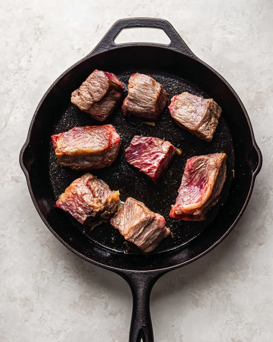 A black cast iron pan sits on a white marbled surface, holding seven pieces of browned meat. The meat pieces vary in size and shape, with some showing visible layers of fat and muscle in reddish-brown and pink colors. The texture of the meat looks slightly seared with some browned edges, and the pieces are spaced apart evenly in the pan. The handle of the pan extends downward in the image. photo taken with an iphone --ar 4:5 --v 7